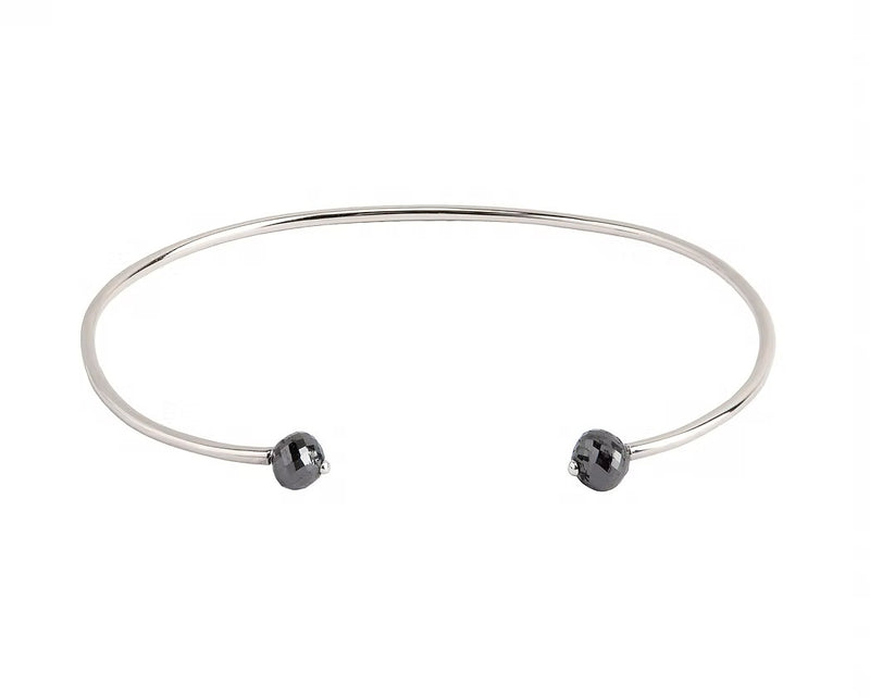 A thin white gold open cuff bangle bracelet with two small faceted grey diamonds at the ends, shown on a plain white background.