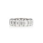 A white gold band ring featuring a row of emerald-cut diamonds, set against a plain white background with a soft reflection.