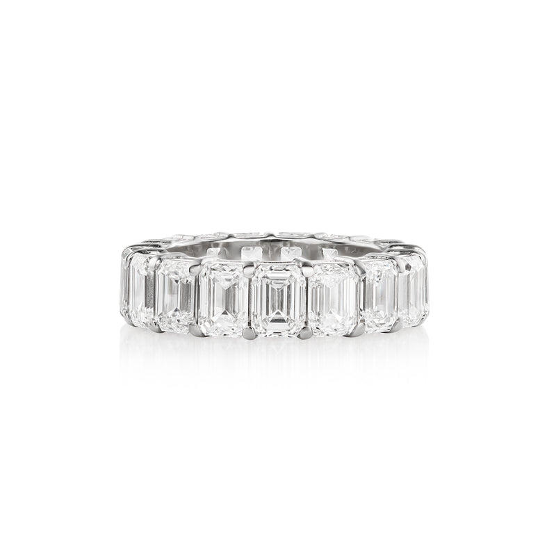 A white gold band ring featuring a row of emerald-cut diamonds, set against a plain white background with a soft reflection.