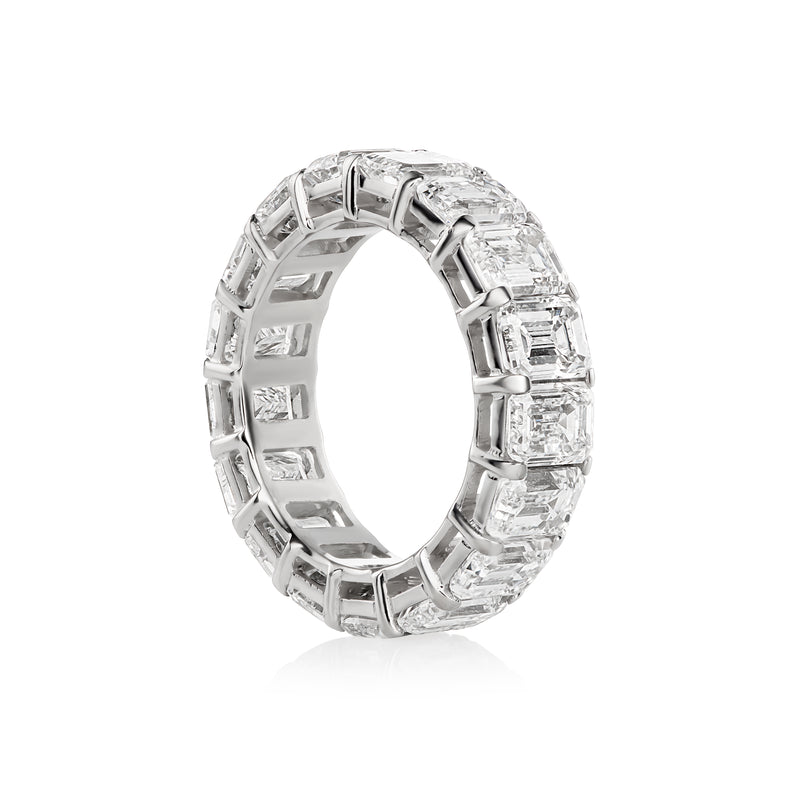 A white gold band ring featuring a row of emerald-cut diamonds, set against a plain white background with a soft reflection.