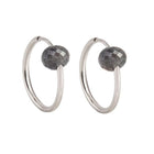 A pair of white gold hoop earrings with a small, faceted dark grey diamond bead attached near the top right of each hoop, shown against a plain white background.