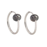 A pair of white gold hoop earrings with a small, faceted dark grey diamond bead attached near the top right of each hoop, shown against a plain white background.