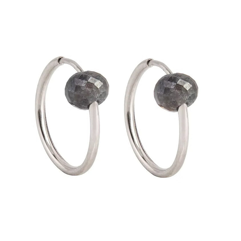 A pair of white gold hoop earrings with a small, faceted dark grey diamond bead attached near the top right of each hoop, shown against a plain white background.