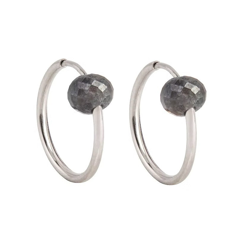 A pair of white gold hoop earrings with a small, faceted dark grey diamond bead attached near the top right of each hoop, shown against a plain white background.