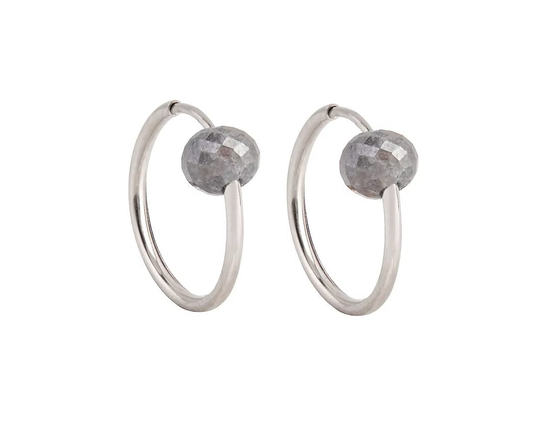 A pair of white gold hoop earrings with a small, faceted dark grey diamond bead attached near the top right of each hoop, shown against a plain white background.