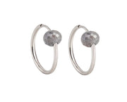 A pair of white gold hoop earrings with a small, faceted dark grey diamond bead attached near the top right of each hoop, shown against a plain white background.