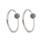 A pair of white gold hoop earrings with a small, faceted dark grey diamond bead attached near the top right of each hoop, shown against a plain white background.