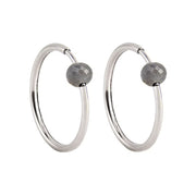 A pair of white gold hoop earrings with a small, faceted dark grey diamond bead attached near the top right of each hoop, shown against a plain white background.