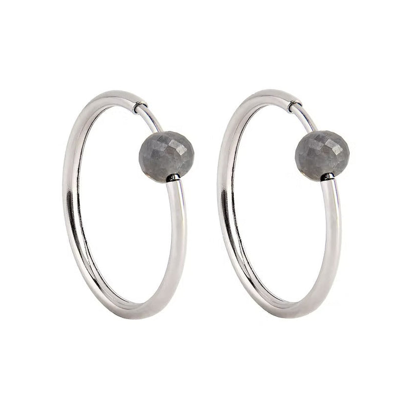 A pair of white gold hoop earrings with a small, faceted dark grey diamond bead attached near the top right of each hoop, shown against a plain white background.