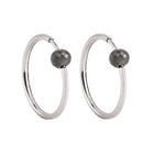 A pair of white gold hoop earrings with a small, faceted dark grey diamond bead attached near the top right of each hoop, shown against a plain white background.