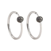 A pair of white gold hoop earrings with a small, faceted dark grey diamond bead attached near the top right of each hoop, shown against a plain white background.