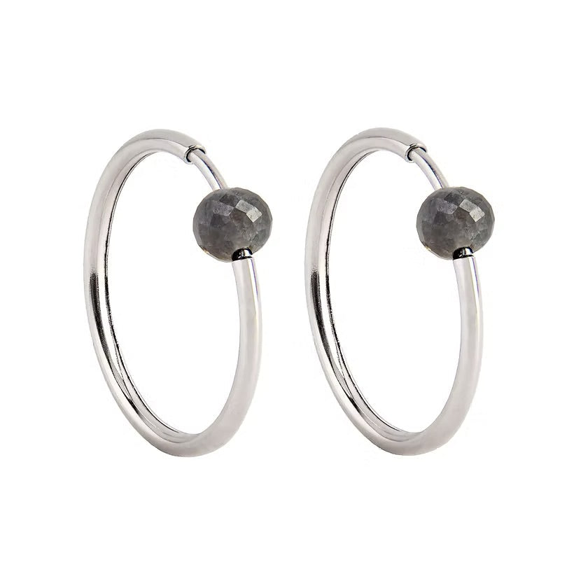 A pair of white gold hoop earrings with a small, faceted dark grey diamond bead attached near the top right of each hoop, shown against a plain white background.