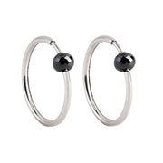 A pair of white gold hoop earrings with a small, faceted dark grey diamond bead attached near the top right of each hoop, shown against a plain white background.