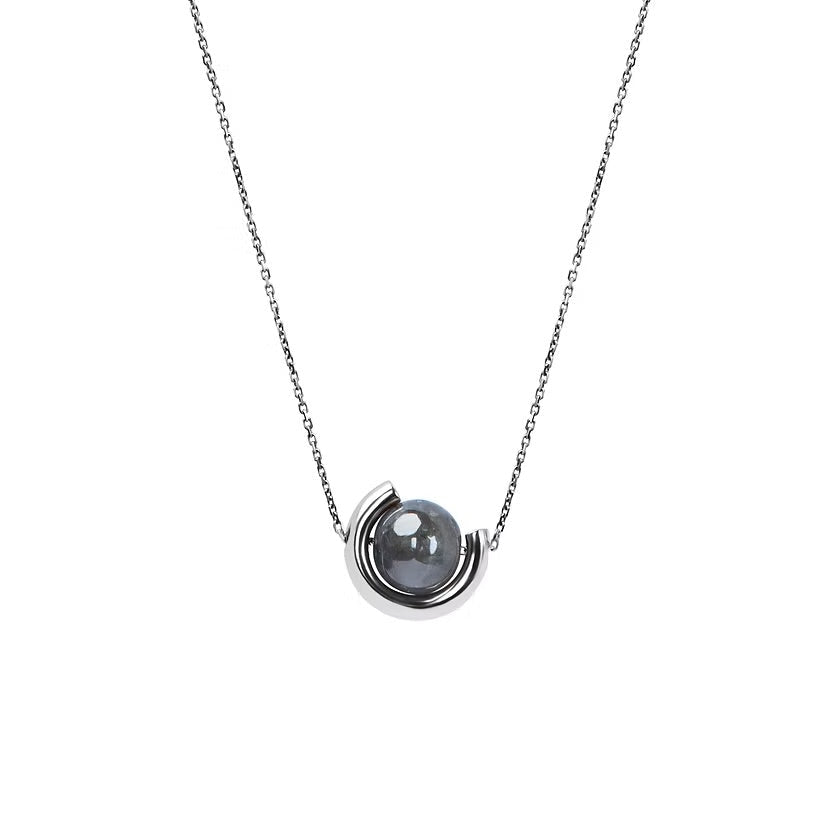A delicate white gold chain necklace featuring a unique crescent-shaped gold pendant cradling a smooth, dark grey diamond, shown against a solid white background.