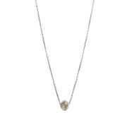 A delicate white gold chain necklace featuring a small, raw, faceted diamond pendant, shown against a solid white background.