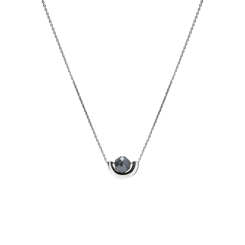 A delicate white gold chain necklace featuring a small, polished gold crescent-shaped setting holding a round, dark gray diamond, presented on a solid white background.