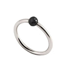 A minimalist white gold ring featuring a single, small, round black faceted diamond, shown on a plain white background.