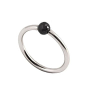 A minimalist white gold ring featuring a single, small, round black faceted diamond, shown on a plain white background.