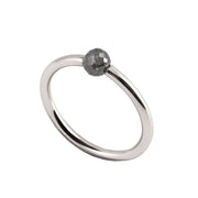 A minimalist white gold ring featuring a single, small, round grey faceted diamond, shown on a plain white background.