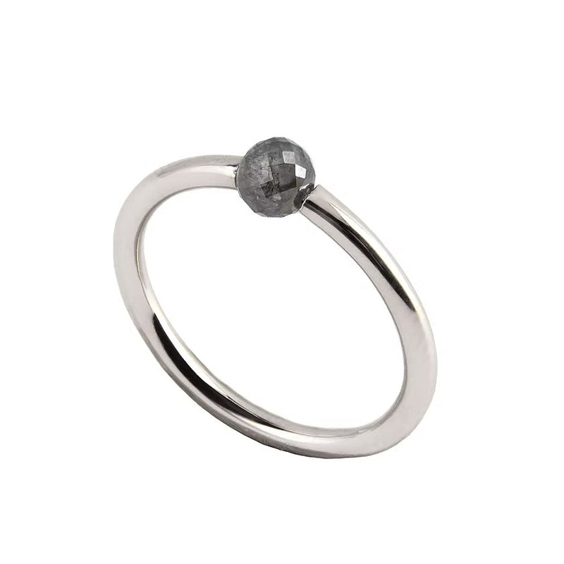 A minimalist white gold ring featuring a single, small, round grey faceted diamond, shown on a plain white background.