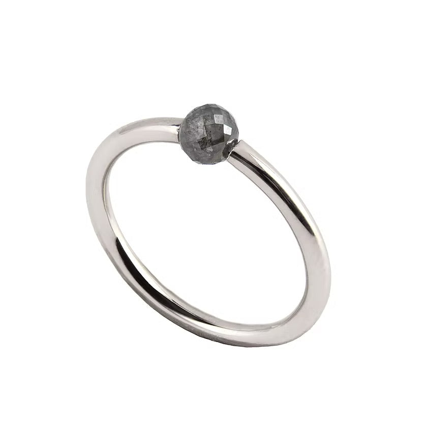 A minimalist white gold ring featuring a single, small, round grey faceted diamond, shown on a plain white background.