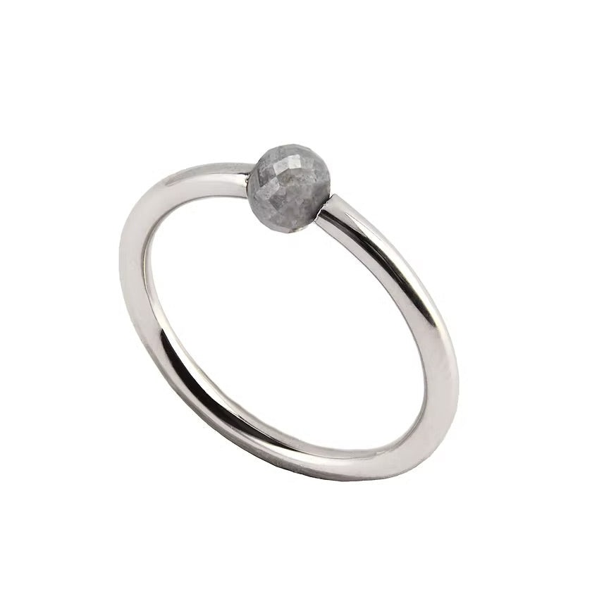 A minimalist white gold ring featuring a single, small, round grey faceted diamond, shown on a plain white background.