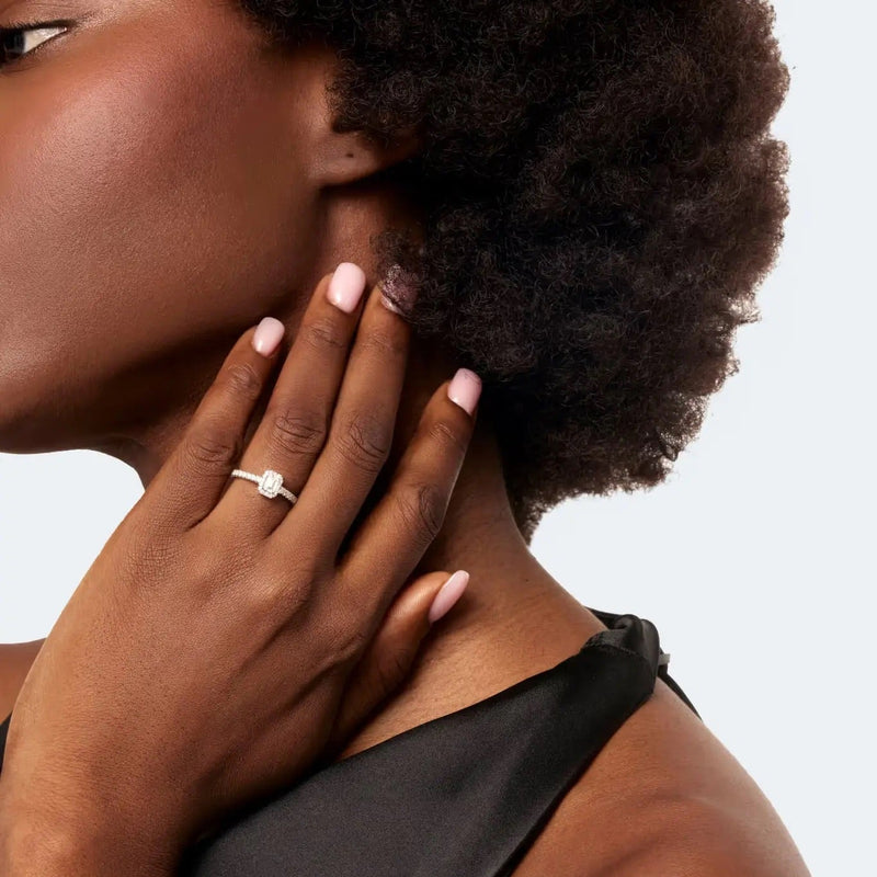 Woman with a ring on her finger touching her neck against a neutral background