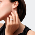 Close-up of a woman wearing a diamond ring on her finger, with a neutral background.