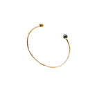 A delicate gold open cuff bracelet with a small dark blue faceted diamonds set in each end, shown on a plain white background.