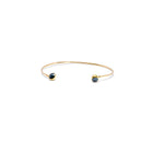 A delicate gold open cuff bracelet with a small dark blue faceted diamonds set in each end, shown on a plain white background.
