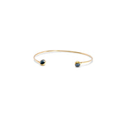 A delicate gold open cuff bracelet with a small dark blue faceted diamonds set in each end, shown on a plain white background.