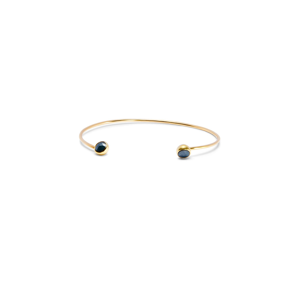 A delicate gold open cuff bracelet with a small dark blue faceted diamonds set in each end, shown on a plain white background.