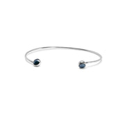 A delicate gold open cuff bracelet with a small dark blue faceted diamonds set in each end, shown on a plain white background.