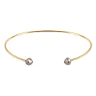 A thin gold open cuff bangle bracelet with two small faceted gray diamonds at the ends, shown on a plain white background.