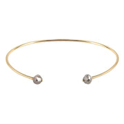 A thin gold open cuff bangle bracelet with two small faceted gray diamonds at the ends, shown on a plain white background.