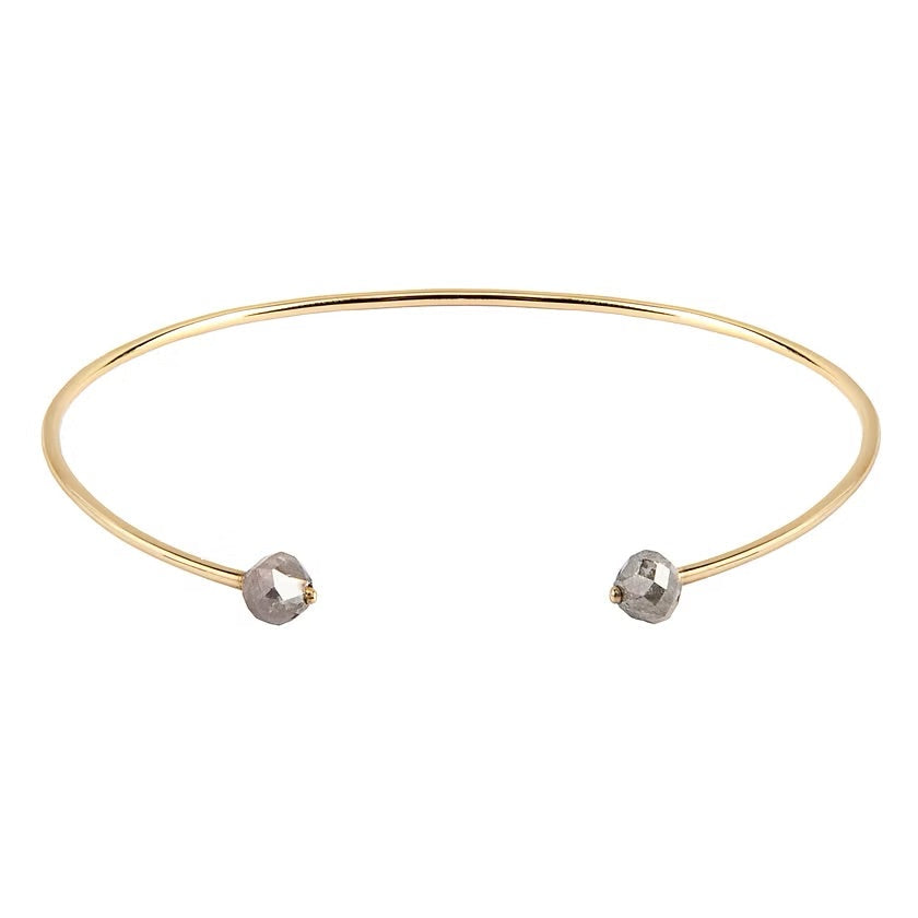 A thin gold open cuff bangle bracelet with two small faceted gray diamonds at the ends, shown on a plain white background.