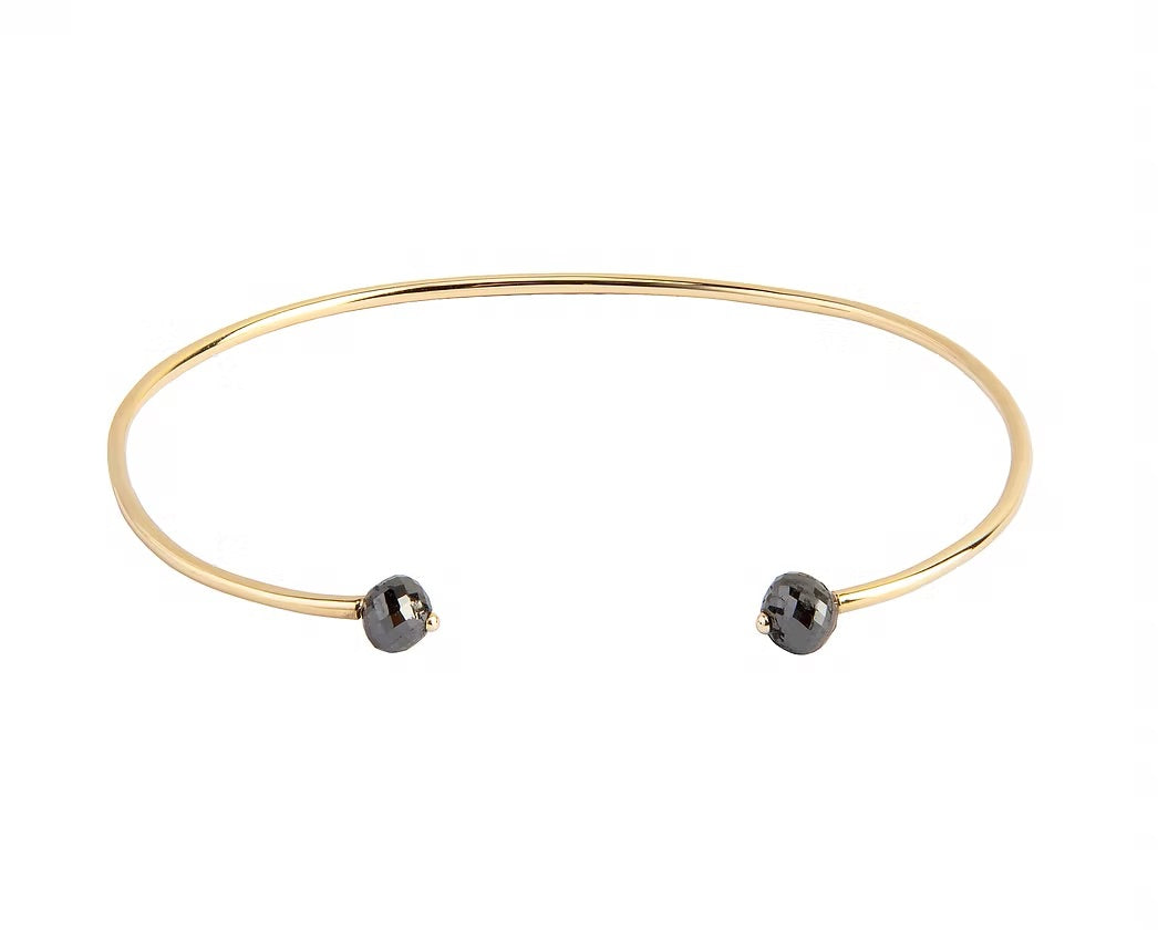 A thin yellow gold open cuff bangle bracelet with two small faceted grey diamonds at the ends, shown on a plain white background.