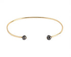 A thin yellow gold open cuff bangle bracelet with two small faceted grey diamonds at the ends, shown on a plain white background.