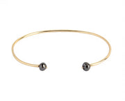 A thin yellow gold open cuff bangle bracelet with two small faceted grey diamonds at the ends, shown on a plain white background.
