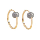 A pair of yellow gold hoop earrings with a small, faceted dark grey diamond bead attached near the top right of each hoop, shown against a plain white background.