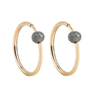 A pair of yellow gold hoop earrings with a small, faceted dark grey diamond bead attached near the top right of each hoop, shown against a plain white background.