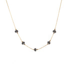A delicate yellow gold chain necklace featuring five small, dark, faceted diamonds spaced along the front, displayed against a solid white background.
