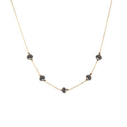 A delicate yellow gold chain necklace featuring five small, dark, faceted diamonds spaced along the front, displayed against a solid white background.