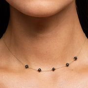 A close-up of a model's neck and collarbone wearing a delicate gold chain necklace with five small, evenly spaced black faceted diamond beads.