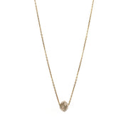 A delicate gold chain necklace featuring a small, raw, faceted diamond pendant, shown against a solid white background.