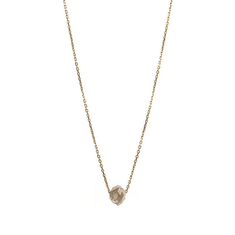 A delicate gold chain necklace featuring a small, raw, faceted diamond pendant, shown against a solid white background.
