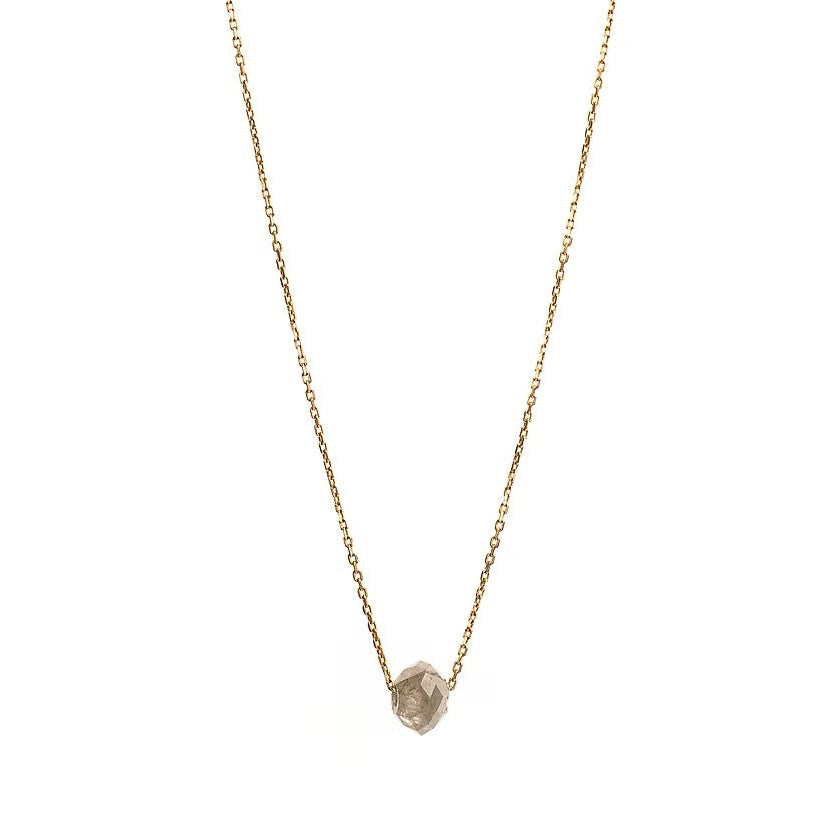 A delicate gold chain necklace featuring a small, raw, faceted diamond pendant, shown against a solid white background.