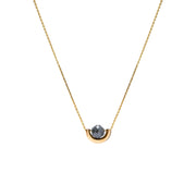 A delicate gold chain necklace featuring a small, polished gold crescent-shaped setting holding a round, dark gray diamond, presented on a solid white background.