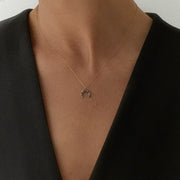 A delicate gold crescent moon pendant necklace with small grey faceted diamonds, worn by a model in a black sleeveless top.