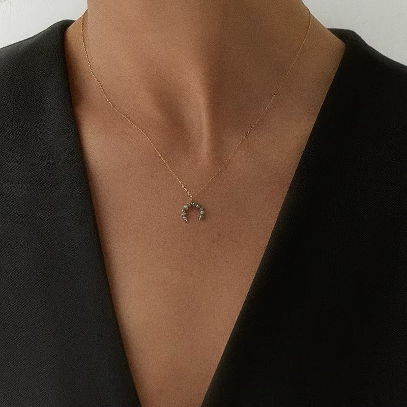 A delicate gold crescent moon pendant necklace with small grey faceted diamonds, worn by a model in a black sleeveless top.
